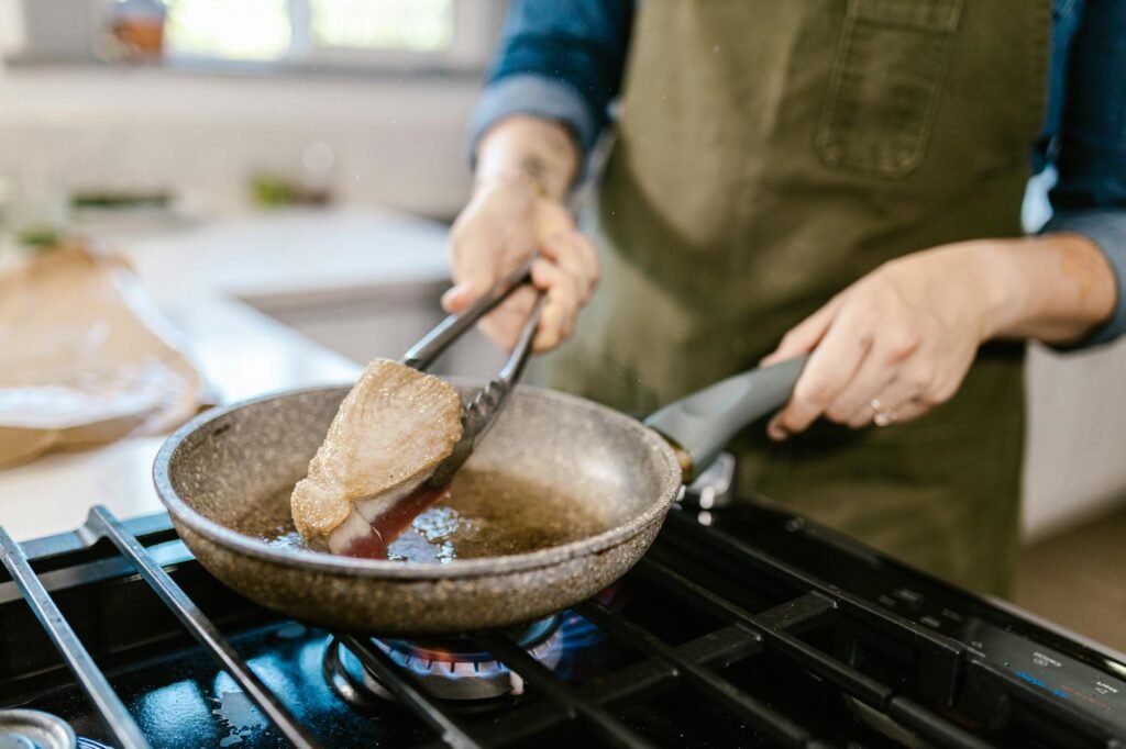 A tidy cooking station with a stainless steel skillet, oil, tongs, and prepared ingredients.