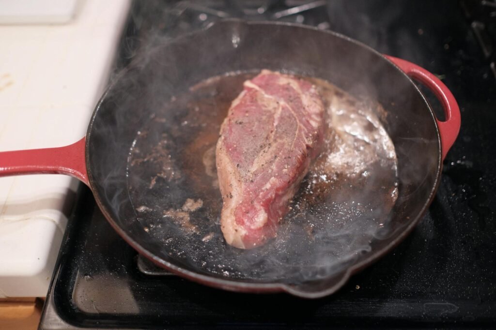A cast iron skillet drying on a stovetop next to a towel and bottle of oil