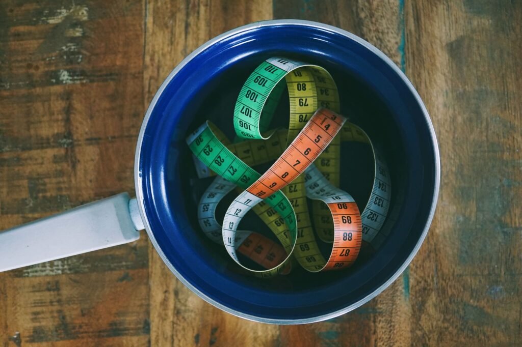 A notebook and tape measure beside a few cookware pieces on a kitchen table.