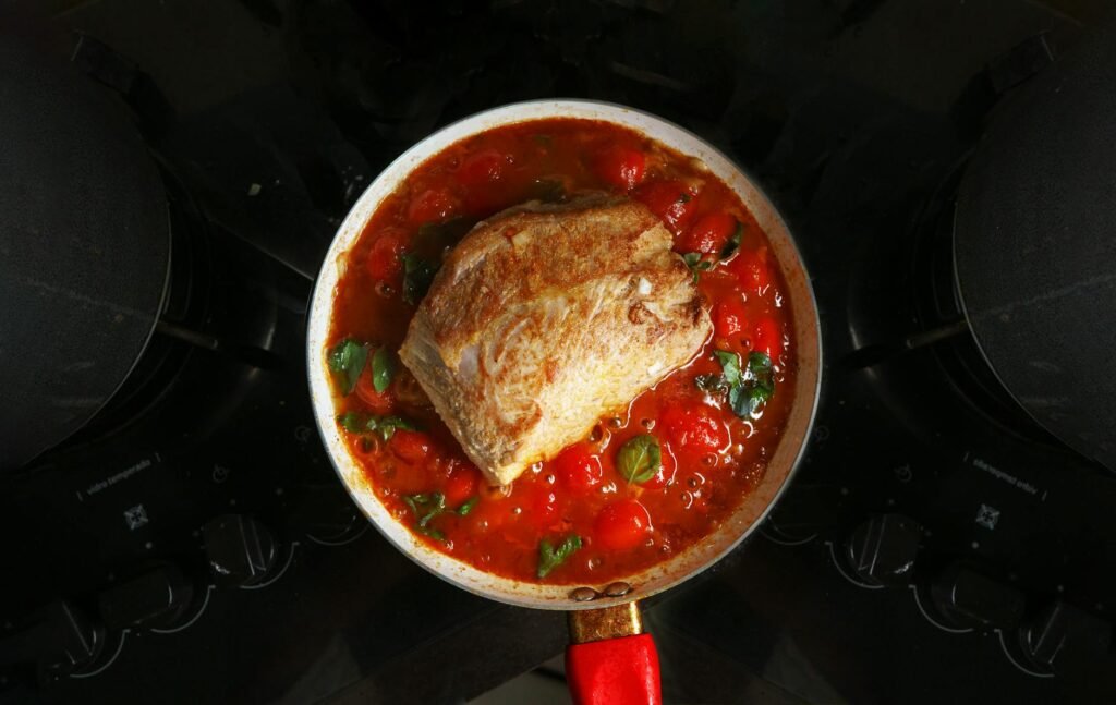 An enameled cast-iron pot simmering a tomato-based dish on a stovetop