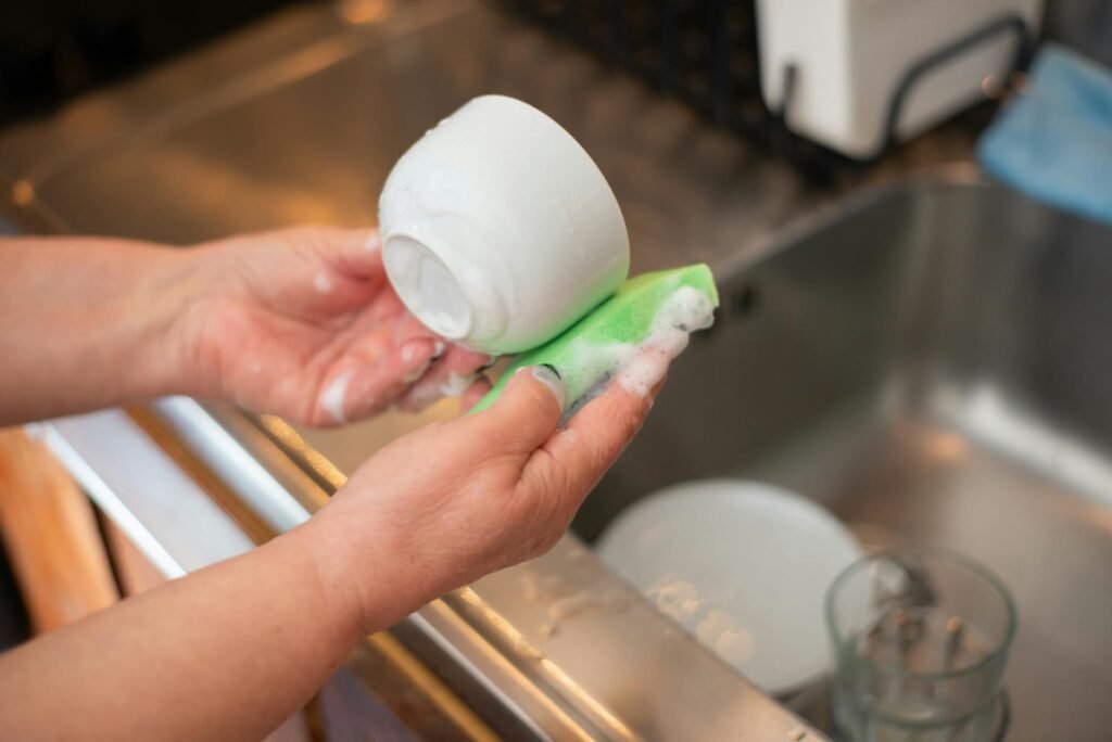 A hand washing a skillet with a soft sponge in a kitchen sink